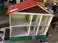 Full view of the wooden doll house with red roof and multiple compartments showing wear.