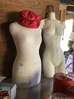 Two female torso mannequins side by side, one fabric-covered with red hat, other plastic, ivory color.