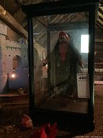 Full view of the monster marionette inside the black wood and glass display case in a dimly lit room with rustic surroundings.