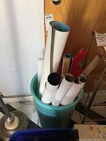 Multiple rolled posters stored in a blue plastic trash bin, including some visible edges of posters in different colors and sizes.