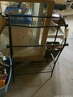 Full view of the metal quilt rack showing three horizontal bars, lower grid shelf, and side curved design.