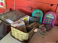 Metal picnic basket filled with 45 RPM records on a table with a red background wall.