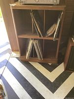 Full view of the vintage solid wood record shelf containing vinyl records on two shelves with visible wear on record sleeves and shelf structure