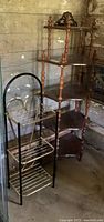 Photo showing both the vintage black metal tiered rack shelf and the solid wood tiered corner shelf with turned spindle supports and crown detail.