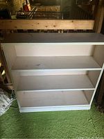 Front view of wooden bookcase with three shelves on green carpet in an indoor setting