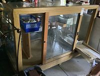 Front view of the vintage wood store display cabinet featuring glass panel sliding doors with a lock, wooden frame, and interior shelving.