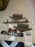 Metal vehicle badges including Loadstar 1800, Loadstar 1600 (damaged), International script, and Sprint M