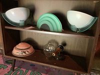 Five vintage Art Deco style light shades and metal and glass sconces displayed on wooden shelves.