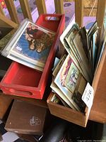 Two wooden trays on a table filled with vintage postcards, one tray painted red and one natural wood.