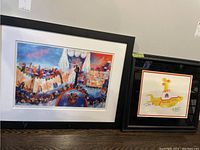 Two framed art pieces side by side on the floor; the larger original Ron Campbell cityscape illustration on the left and the smaller Yellow Submarine print on the right.