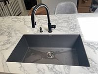 Top view of rectangular undermount sink with matte dark gray finish installed in marble countertop along with black high arc faucet with lever handle and spray function