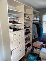 White closet shelving unit with multiple shelves and three drawers visible in the front. Unit is installed against the wall with various clothing items and shoe boxes around it.