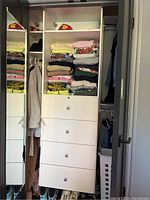 Front view of the white closet shelving unit with five drawers, some shelves containing folded clothes (not included).