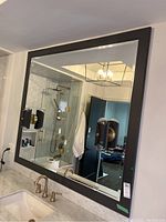 Large black framed rectangular bathroom mirror mounted above sink with two light fixtures attached vertically on opposite frame sides.