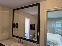 Full view of large rectangular framed mirror above bathroom sink, showing reflection of room and the attached lights.
