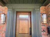 Two outdoor wall sconces mounted on either side of a front door with brick and painted trim