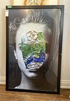 Close-up photo of framed photo art with crushed can covering central part of face in the portrait.
