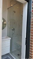 Front view of glass shower door fully installed with chrome handle and hinges visible, marble wall tiles behind
