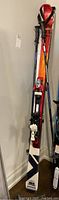 Photos showing a pair of Salomon skis with bindings and Rossignol ski poles leaning against a wall.