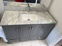Front angled view of gray bathroom vanity showing marble top, sink and faucet