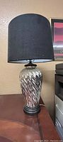 Front view of the desk lamp with grey textured ceramic base and black fabric lampshade on a wooden surface, showing overall form and design.