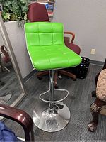 Green cushioned swiveling bar stool chair with chrome base and footrest in room with other chairs