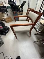 View of one wooden lounge chair with grey upholstered seat and backrest, medium brown wooden frame and armrests.