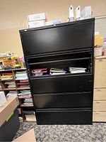 Full front view of the large black metal file cabinet showing all five drawers closed except one open with files inside.