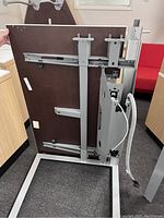 Underside of large desk showing metal support frame, integrated power outlet box, and cable conduit management system.