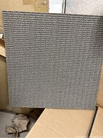 Single grey modular carpet tile with textured surface shown outside packaging.