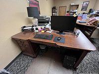 Front view of dark brown wooden desk with multiple drawers and office items on top, showing condition and drawer design.