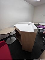 Side view of receptionist corner desk showing white top with hole for cables and light wood laminate body with open shelves.