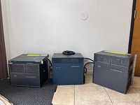 Three Cisco Catalyst 6000 series modules side by side: two power supply modules (left and right) and one Supervisor Engine module (center) with coiled cable on top