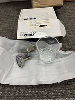Photo showing chrome-finished metal tumbler holder and clear octagonal glass tumbler alongside the original Kohler box and protective wrapping.