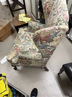 Side view of vintage wingback chair showing floral fabric upholstery, gently curved arm on wooden legs.