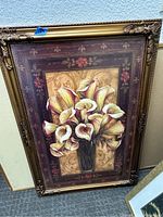 Framed floral painting featuring calla lilies in a black vase on a decorative background.