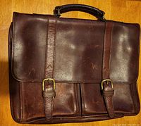 Front view of the brown Aston leather briefcase showing buckle straps and handle