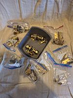 Top-down view of all items showing brass doorknobs in a gray container and several plastic bags filled with assorted door hinges and hardware components spread on a fabric surface.