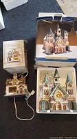 Two ceramic Christmas village buildings shown with respective boxes; church is larger with green roofs, school smaller with Christmas decorations and electrical plug