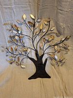 Full front view of the metal tree wall art showing the black trunk and branches and metallic gold and copper textured leaves.