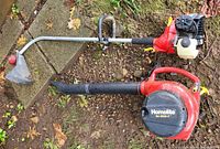 Two items laid on the ground: a red-black Homelite Vac Attack II leaf blower and a Mighty Lite 26cc weedwacker with curved shaft and guard.