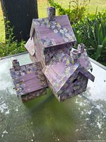 Wooden birdhouse with 5 connected compartments, each with pitched roofs and chimneys, painted purple with white and yellow floral patterns.