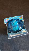 Blue spherical Mega Ball ice cream maker in original packaging, partially open showing the product inside.