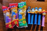 Photo showing a total of 8 PEZ dispensers, including 3 unopened in packaging and 5 loose dispensers featuring Donald Duck and other Disney characters.