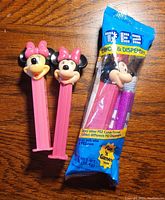 Photo showing two opened Minnie Mouse PEZ dispensers and one unopened dispenser in original blue PEZ candy packaging with Mickey Mouse image.