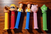 Photo of 6 opened PEZ dispensers with Pixar movie characters on wooden surface.