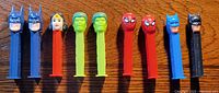 Nine PEZ superhero candy dispensers arranged in a row on a wooden surface.