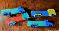 Four PEZ truck toys arranged on a wooden surface, showing various color combos with six wheels each, including turquoise with blue, yellow with blue, green with red and turquoise with blue trucks.