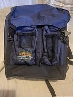 Front view of the navy blue Rak Gear Wickford backpack showing two mesh front pockets with drawstring closures and the Rak logo patch.