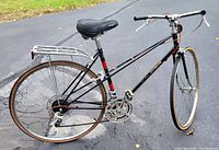 Side view of vintage black Motobecane Mirage Mixte bicycle showing frame, replacement black saddle, drop handlebars, tires, and rear rack.